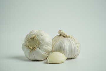 Fresh white garlic bulbs and a single peeled clove, ready for culinary use, resting on a clean studio white background, showcasing natural texture and vibrant appeal for cooking