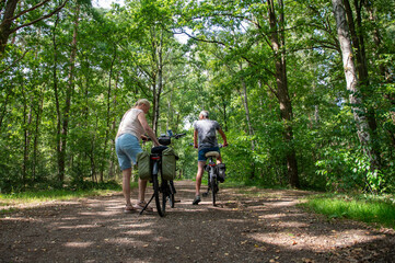 Obraz premium Senior couple pausing their cycling tour on a shaded path, surrounded by lush green trees, enjoying an active lifestyle and harmonious moments together in nature