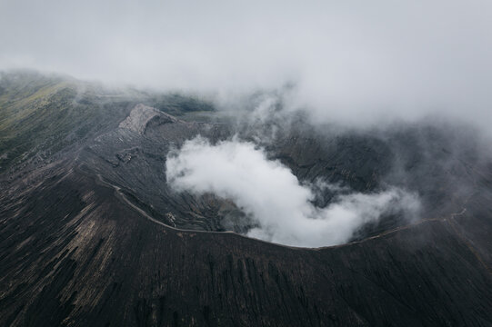 Aerial view of the Bromo volcano crater, where wisps of cloud dance with the dark volcanic rock, creating an ethereal dance of light and shadow, Mt. Bromo, East Java, Indonesia.