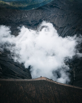 Aerial view of ethereal clouds swirling within the volcanic caldera of Mt. Bromo, a symphony of muted grays and browns against the stark white, Mt. Bromo, East Java, Indonesia.