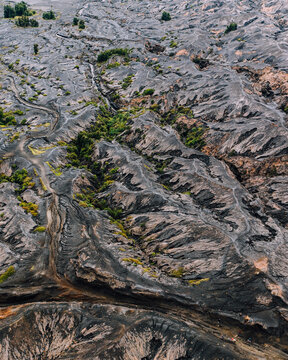 Aerial view of a stark, volcanic landscape etched with winding paths and sparse vegetation, a tapestry of grey and green textures, Mt. Bromo, East Java, Indonesia.