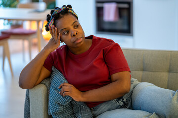 Pensive frustrated black woman sitting on sofa at home feeling uneasy, distracted. Thoughtful...