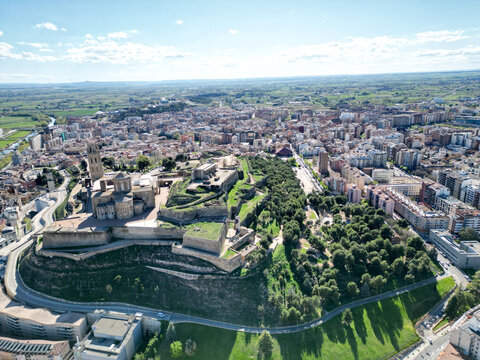 Aerial view of the Seu Vella cathedral and Castell del Rei standing majestically above the city, contrasting with the verdant trees and distant buildings, Lleida, Spain.