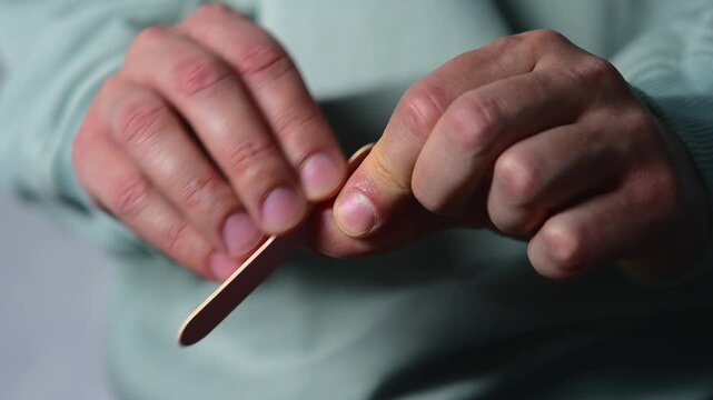 Trimming and filing nails with a nail file.
A man trims his long fingernails and files the sharp edges with a nail file.