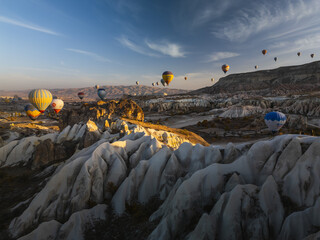 Aerial view of vibrant hot air balloons drifting over the surreal, sculpted landscapes of Cappadocia, painted in hues of dawn, Goreme, Nevsehir, Turkiye.