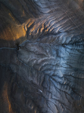 Aerial view of the stark, lunar-like landscape, where shadows deepen the rugged terrain's texture, contrasting the golden light, Goreme, Nevsehir, Turkiye.