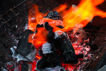Close-up of burning charcoal with bright orange flames in a barbecue grill.