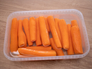 Peeled fresh carrots soaked in water in a plastic container, preparation for cooking or storage in the kitchen.