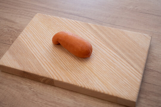 Single sausage placed on a wooden cutting board on a kitchen table, traditional Czech and Slovak style sausage used for grilling or cooking.
