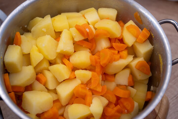 Boiled potatoes and carrots in a stainless steel pot, prepared for baking traditional French-style potatoes or layered dishes.