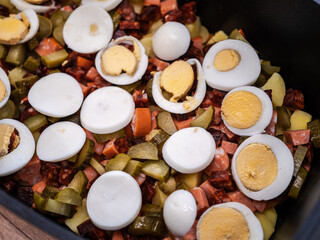 Preparation of traditional French potatoes with sausage, eggs, and pickles in a black baking dish before baking. Homemade Slovak comfort food.