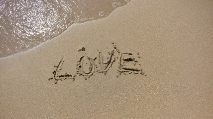 Love word is written on sand and soft sea wave next to it top view
