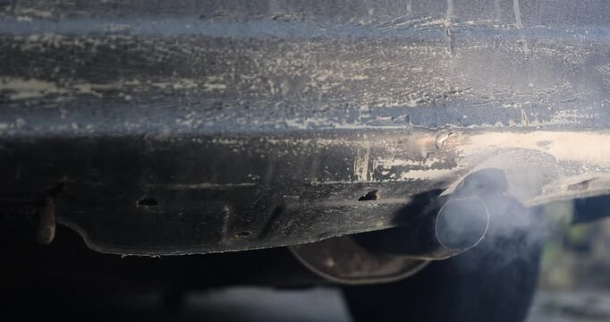 gray harmful smoke from the muffler of a car with an inoperable or not installed filter for cleaning exhaust gases, an old pipe in the car for releasing exhaust gases from the car engine
