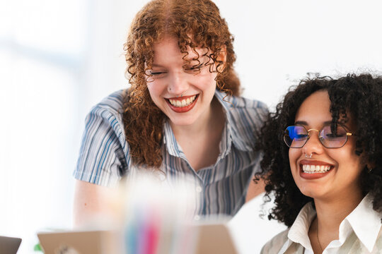 Two young women share a laugh while working together on a project, their smiles conveying a sense of camaraderie and shared success.