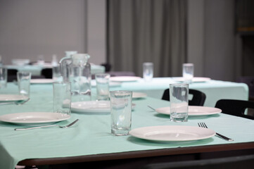 Table setting with white plates and glasses on a mint green tablecloth