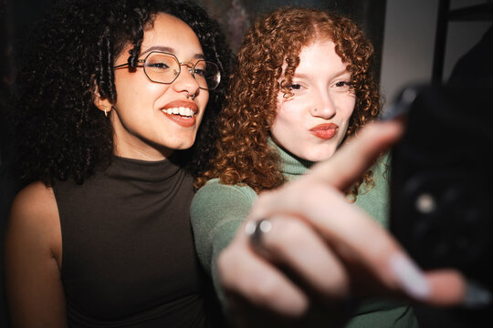 Two young women with curly hair take a selfie together, one smiling and the other pouting playfully.
