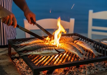 Chef grilling whole fish over open flames on a barbecue at night, with chairs in the background