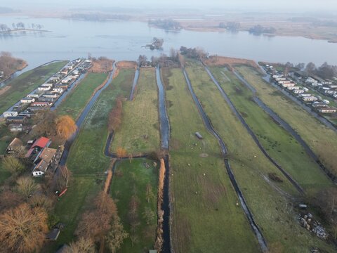 Aerial view of canals cutting through vibrant green meadows, reflecting the soft morning light between rows of quaint houses, Giethoorn, Overijssel, Netherlands.