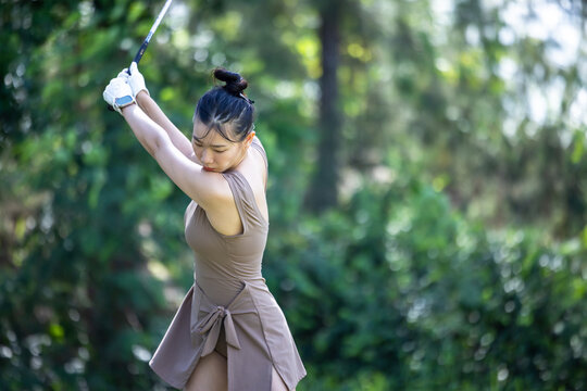 Asian woman practices golf swing on driving range, Asian woman play golf in golf driving range, Asian woman to play golf leisure and relaxation. - Powered by Adobe