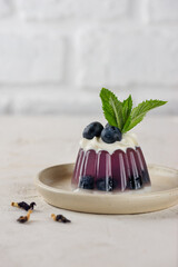 Purple jelly with fresh blueberries, mint, anchan tea and coconut cream with agar agar in a plate. Summer dessert, gelatin free. Vertical orientation.