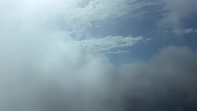 An immersive pilot’s perspective from the cockpit of a jet airplane flying peacefully through ethereal broken stratus clouds under a deep blue sky.