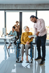 Business woman in wheelchair working with colleague in modern inclusive office. Diversity, support