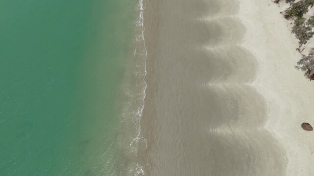 Drone shot of turquoise waves rolling gently onto the pristine sandy shores of the Bijag&oacute;s Islands in Guinea-Bissau, aerial top down