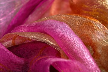 A close-up of vibrant silk fabric in shades of pink, orange, and gold, showcasing intricate textures.