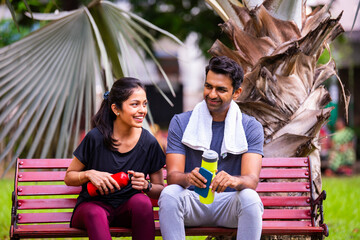 Indian beautiful young couple chatting post fitness relaxing together in morning park