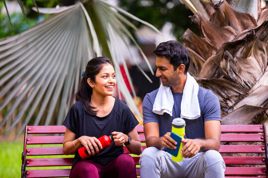 Indian beautiful young couple chatting post fitness relaxing together in morning park