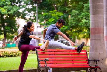 Indian beautiful young couple stretching post workout relaxing together in park outdoors