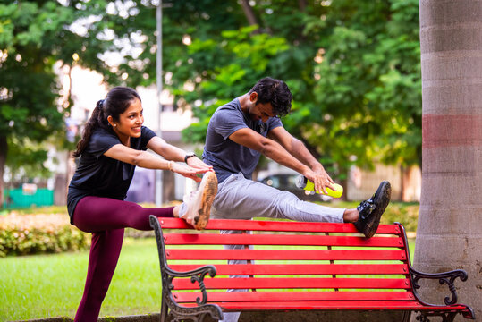 Indian beautiful young couple stretching post workout relaxing together in park outdoors