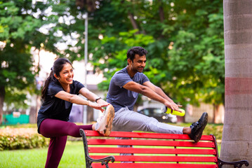 Indian beautiful young couple stretching post workout relaxing together in park outdoors