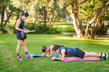 Personal trainer coaching couple doing plank exercise in park