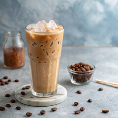 Iced coffee in tall glass placed on marble coaster surrounded by coffee beans and ice, minimal caffeine drink setup on gray background with overhead lighting