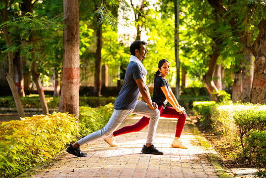 Indian beautiful young couple stretching post workout relaxing together in park outdoors