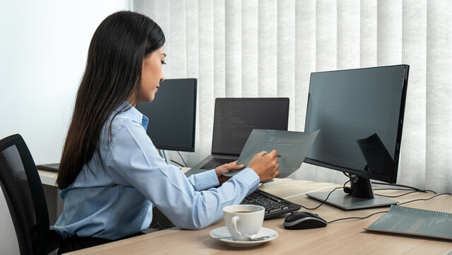 Female programmer reading document of database code to thinking for website development while using multiple