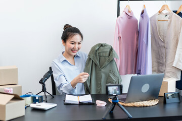 Female fashion designer showing clothes to sell and recording videos for streaming on her blog while checking order