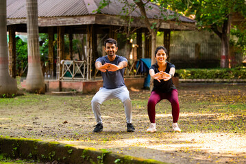 Obraz premium Indian beautiful young couple doing squats together during outdoor workout in sunny park