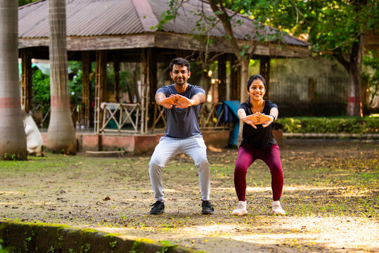 Indian beautiful young couple doing squats together during outdoor workout in sunny park