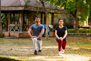 Naklejka premium Indian beautiful young couple stretching post workout relaxing together in park outdoors