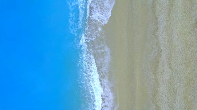 Waves gently lapping against sandy beach with smooth texture and bright blue sea under clear sky, creating peaceful coastal background