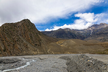 Rocky Mountains and dry river valley in Upper Mustang, Nepal. A dramatic Himalayan landscape with barren hills and the flowing riverbed, showcasing the rugged beauty of the high-altitude desert.