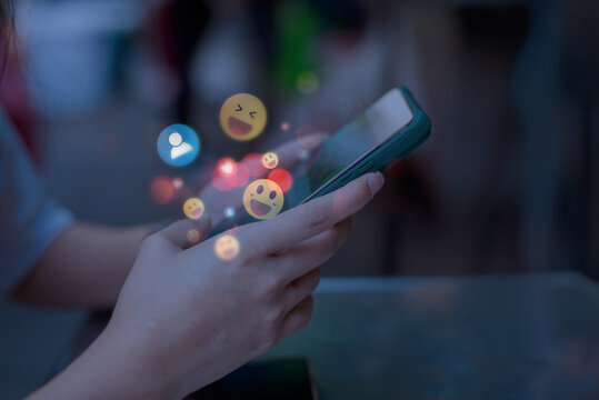 Close-up of hands holding a smartphone with floating social media emojis, representing online communication, messaging, and digital interaction.