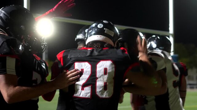 American football team celebrating touchdown together at night