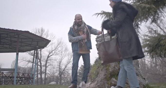 A couple enjoys a peaceful autumn walk in the park, stopping to explore a unique rock formation.