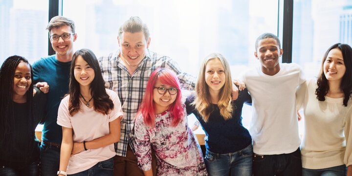 Diverse group of young students smile together in classroom. Happy student friends smile, diverse group arms around together, friendly atmosphere. Happy diverse young students friends group smile