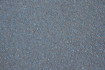 Rough, speckled asphalt surface with tiny pebbles and subtle blue tint