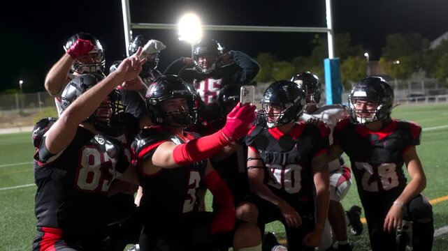 American football players taking a team selfie on the field at night