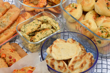 A close-up displays an appetizing spread of baked savory items in glass bowls, including mini pizzas, flatbreads, crackers with parsley, and rolls with Parmesan and garlic, alongside gorgonzola buns a
